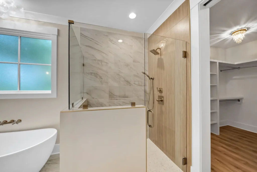 Walk-in shower with glass enclosure, pale wall tile and brass fixtures